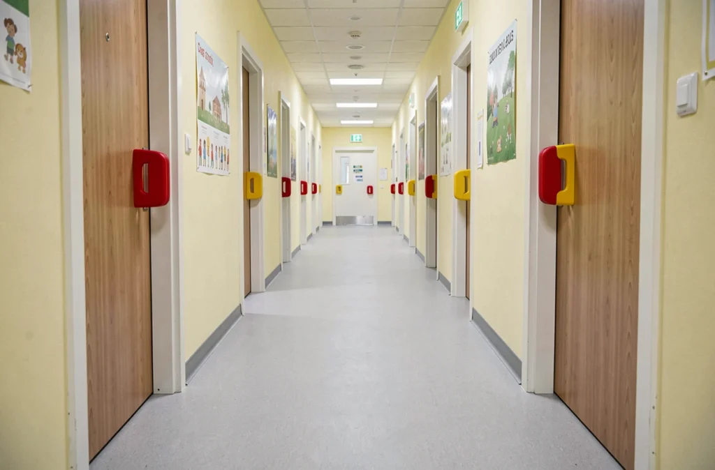 Couloir d'établissement d'accueil pour enfants équipé de protège-doigts anti-pince colorés sur plusieurs portes, vue large montrant les dispositifs de sécurité conformes aux normes 2026