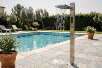 Douche solaire moderne installée en bord de piscine avec carrelage en pierre grise et plantes méditerranéennes