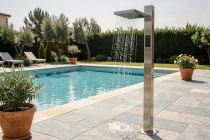 Douche solaire moderne installée en bord de piscine avec carrelage en pierre grise et plantes méditerranéennes