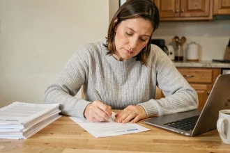 Femme remplissant des formulaires administratifs de changement d'adresse à une table de cuisine en bois
